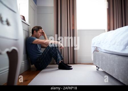 Deprimiert Mann mit Schlafanzug sitzen auf dem Boden des Schlafzimmers Stockfoto