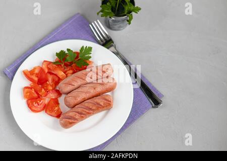 Frühstück mit Würstchen und Gemüse. Tomaten in Scheiben geschnitten. Auf einem hellen Hintergrund. Stockfoto