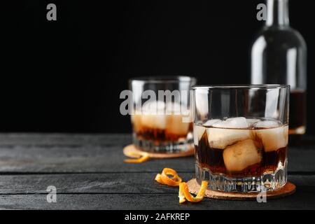 Gläser Whiskey mit Orangenschalen und Eis auf Holz- Hintergrund mit Flasche, Platz für Text Stockfoto