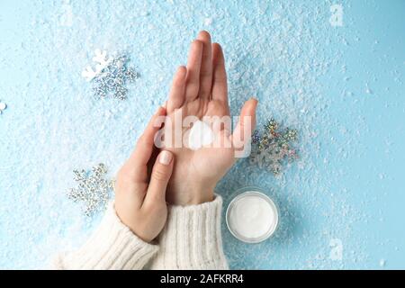 Frau Hände, feuchtigkeitsspendende Creme im Winter, Herzform aus Creme auf verschneiten blauen Hintergrund erstellt, Nahaufnahme. Ansicht von oben Stockfoto