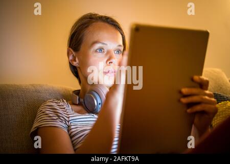 Hübsche, junge Frau, die zu Hause in den Abend arbeiten - mit Ihren Tablet-PC sowie Bluetooth® Kopfhörer, schreiben Sie einige Ideen für morgen Stockfoto