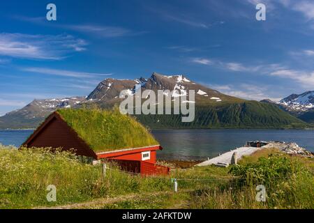 BAKKEJORD, INSEL KVALØYA, NORWEGEN - Rasen Dach Gebäude auf der Insel Kvaløya im Vordergrund, und Straumsfjorden Blick auf Fjord und Berge. Stockfoto