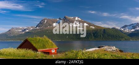 BAKKEJORD, INSEL KVALØYA, NORWEGEN - Rasen Dach Gebäude auf der Insel Kvaløya im Vordergrund, und Straumsfjorden Blick auf Fjord und Berge. Stockfoto