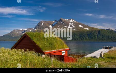 BAKKEJORD, INSEL KVALØYA, NORWEGEN - Rasen Dach Gebäude auf der Insel Kvaløya im Vordergrund, und Straumsfjorden Blick auf Fjord und Berge. Stockfoto