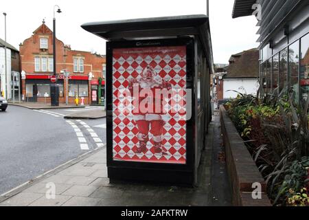 Coca Cola Santa Claus hält klassische Coca-Cola-Flaschen auf Bushaltestelle Anzeige, Leatherhead Stadt, Surrey, Großbritannien, 2019 Stockfoto