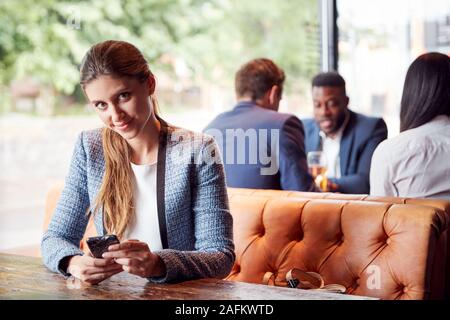 Portrait der Unternehmerin Sitzen in Bar Kontrolle Handys während Kollegen Treffen für Getränk Stockfoto