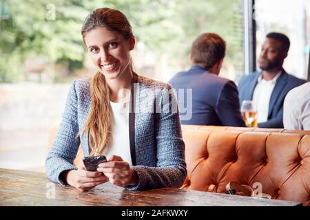 Portrait der Unternehmerin Sitzen in Bar Kontrolle Handys während Kollegen Treffen für Getränk Stockfoto