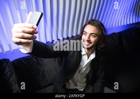 Glückliche junge eleganten Mann mit Smartphone, selfie auf der Couch in der Nacht Club Stockfoto