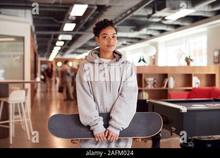 Portrait von Leger gekleidete junge Geschäftsfrau mit Skateboard In Offenen Arbeitsplatz stehen Stockfoto