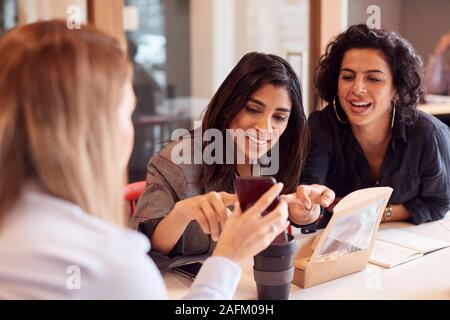 Gruppe von jungen Unternehmerinnen Sitzen um den Tisch, Arbeitsessen und Mobiltelefone Stockfoto