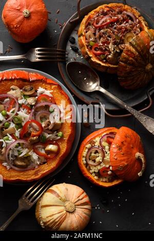 Gesundes Fleisch essen. Große und kleine Kürbisse, gefüllt mit braunen und weißen Reis, pearl Couscous, Erbsen, Champignons, Paprika und Zwiebel auf Schwarz backgroun Stockfoto