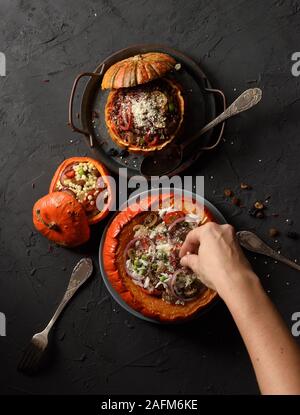 Schlanke Frau Hand gießen geriebenen Käse auf Kürbis gefüllt mit Reis, Champignons und Zwiebeln und kleinere Kürbisse mit rotem Reis und Pearl couscous auf b Stockfoto