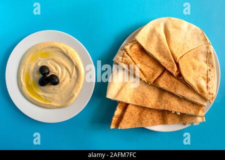 Berühmte traditionelle arabische Küche - Tahini Sosse mit Fladenbrot auf blauem Hintergrund. Flach, Ansicht von oben. Hummus mit Oliven und Fladenbrot. Stockfoto