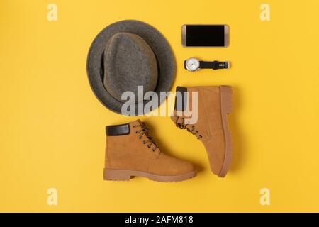 Layout der Herbst Kleidung und Accessoires in warmen Farben auf einem gelben Hintergrund. Hut, Stiefel, Telefon und schauen Sie sich flach in der Nähe. Stockfoto