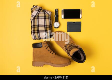 Layout der Herbst Kleidung und Accessoires in warmen Farben auf einem gelben Hintergrund. Shirt, Stiefel, Telefon und schauen Sie sich flach in der Nähe. Stockfoto