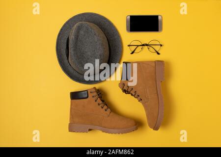 Layout der Herbst Kleidung und Accessoires in warmen Farben auf einem gelben Hintergrund. Jeans, Hemd, Schuhe, Telefon und schauen Sie sich flach in der Nähe. Stockfoto