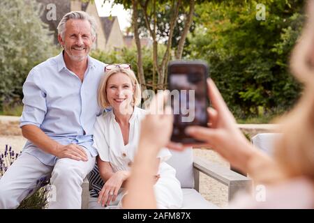 Erwachsene Tochter unter Bild von älteren Eltern sitzen im Garten am Handy Stockfoto
