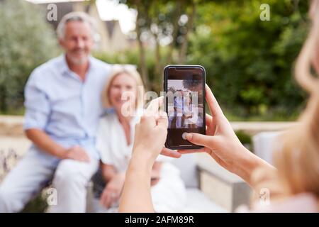 Erwachsene Tochter unter Bild von älteren Eltern sitzen im Garten am Handy Stockfoto