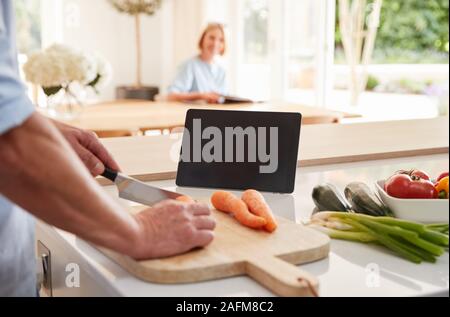 Ältere Menschen folgende Rezept auf digitalen Tablette wie Frau sitzt am Esstisch Eine liest Magazin Stockfoto