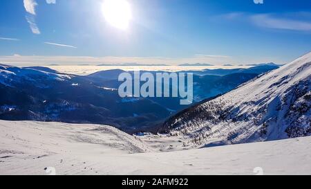 Eine Winterlandschaft der Berge. Sonne scheint in den Himmel. In den Bergen hängen vollständig abgedeckt mit einer dicken Schicht Schnee. Wenige Bäume auf der Piste. Stockfoto