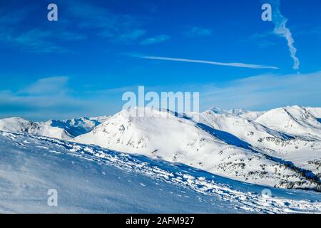 Eine Winterlandschaft der Berge. Sonne scheint in den Himmel. In den Bergen hängen vollständig abgedeckt mit einer dicken Schicht Schnee. Wenige Bäume auf der Piste. Stockfoto