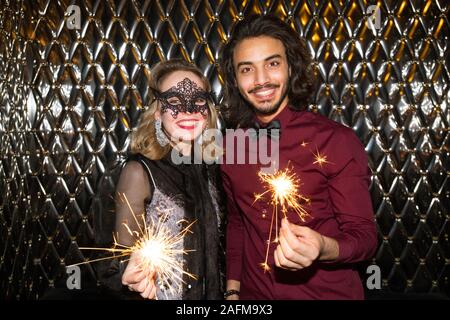 Happy girl in venezianische Maske und Guy mit funkelnden bengalischen Lichtern an Sie Stockfoto