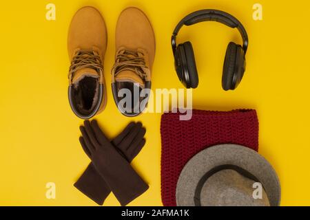 Layout der Herbst Kleidung und Accessoires in warmen Farben auf einem gelben Hintergrund. Handschuhe, Kopfhörer, Schuhe, Mütze und Schal flach in der Nähe. Stockfoto