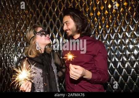 Lächelnde Mädchen in venezianische Maske und ihr Freund holding Sekt Bengal lights Stockfoto