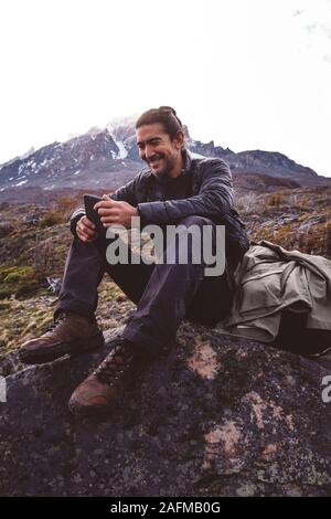 Happy Wanderer sitzen auf Stein in den Bergen sein Telefon prüfen Stockfoto