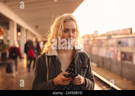 Junge Frau mit Smart Phone beim Warten auf die Bahn Stockfoto
