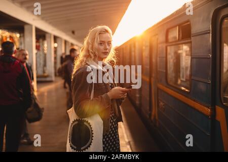 Junge Frau mit smart phone stehend an der U-Bahn Station Stockfoto