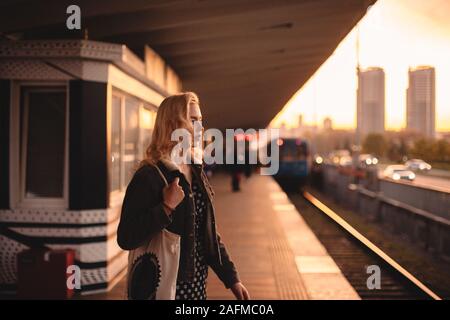 Nachdenkliche junge Frau wartet auf Zug in der Nähe der U-Bahn Station bei Sonnenuntergang Stockfoto