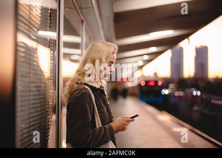 Junge Geschäftsfrau mit Smart Phone beim Warten auf die U-Bahn Stockfoto