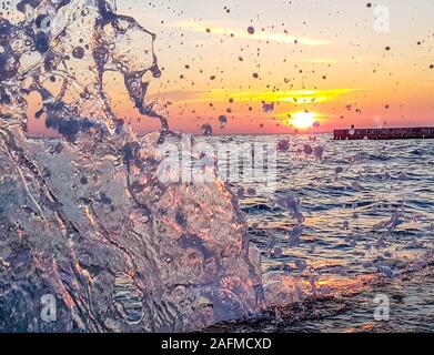 Romantischer Sonnenuntergang durch eine steinige Hafenpromenade. Die Sonne über dem Horizont. Die Sonnenstrahlen in das ruhige Meer widerspiegelt. Steinigen Ufer ist von den Wellen weggespült, s Stockfoto