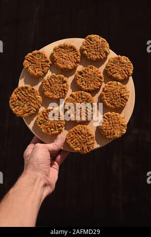 Gesund vegan Glutenfrei Süßigkeiten. Hand mit hausgemachten Haferflocken Cookies mit Kürbiskernen auf runden Board auf schwarzem Hintergrund Kopie Raum Stockfoto