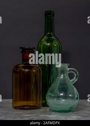 Grünen und braunen Glasflaschen mit Jar auf Marmor tisch mit schwarzem Hintergrund noch Leben Stockfoto