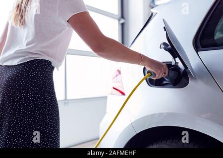 Nahaufnahme von Frau Laden Elektrofahrzeug mit Kabel in der Garage zu Hause Stockfoto