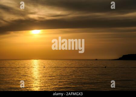 Romantischer Sonnenuntergang von einem Strand. Die Sonne über dem Horizont. Die Sonnenstrahlen in das ruhige Meer Gewässern widerspiegelt. Es ist eine Insel, auf der Seite. Wenige Vögel Stockfoto