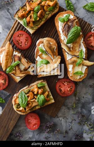 Gebratene Pilze. Genießbare Steinpilze und Pfifferlinge auf Sandwiches mit Basilikum und Tomaten auf dunklem Hintergrund der Ansicht von oben kopieren. Low Key sti Stockfoto