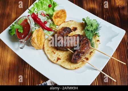 Gesunden gegrilltes mageres gewürfelten Schweinefleisch Kebabs serviert mit Mais-Tortilla und frischem Salat und Tomaten-Salat, Nahaufnahme auf dunklem Hintergrund Stockfoto