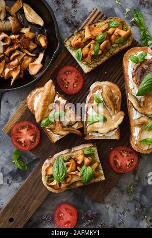 Bruschetta mit gebratenen Pfifferlingen und Steinpilzen, Tomaten und Basilikum auf dunklem Hintergrund der Ansicht von oben kopieren. Low Key noch Leben mit Na Stockfoto