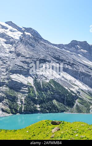 Vertikale Foto von erstaunlichen Oeschinensee See in der Nähe von Kandersteg in der Schweiz. Türkisfarbenen See von steilen schneebedeckten Bergen umgeben. Touristische Ort in den Schweizer Alpen. Sommer Alpine Landschaft. Stockfoto