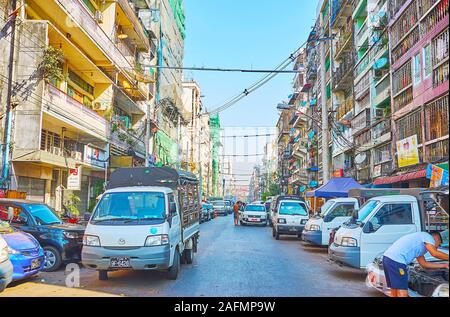 YANGON, MYANMAR - 17. FEBRUAR 2018: die lebendigen Straßen von Chinatown mit schäbigen Gebäuden erkunden, vielen geparkten Autos, kleine Stände und Straßencafés, Stockfoto