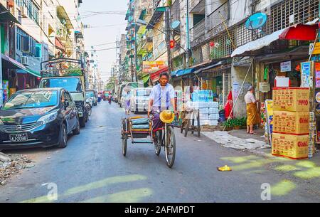 YANGON, MYANMAR - Februar 17, 2018: Die städtische Szene in Chinatown mit parkenden Autos und Rikscha, Reiten entlang des heruntergekommenen Gebäuden, am 17. Februar in Stockfoto