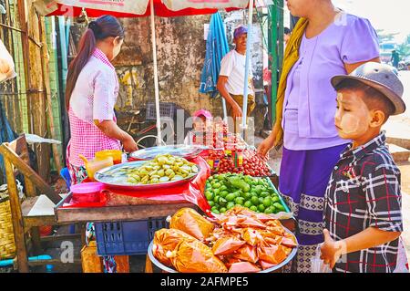 YANGON, MYANMAR - Februar 17, 2018: Die Kunden im Chinatown Marktstand, Verkauf von frischen Pflaumen und Gewürzen, am 17. Februar in Yangon Stockfoto