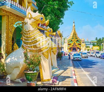 YANGON, MYANMAR - 17. FEBRUAR 2018: Die vergoldeten Chinthe Lions des Yahandar Theindawgyi Tempel der Shwedagon Pagoda Road Gesicht mit starken Verkehr und ornat Stockfoto