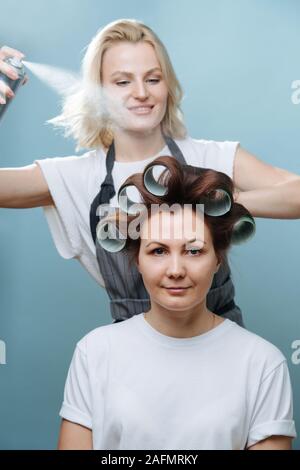 Stylistin Frau spritzen Client braunes Haar auf Rollen über Blau Stockfoto