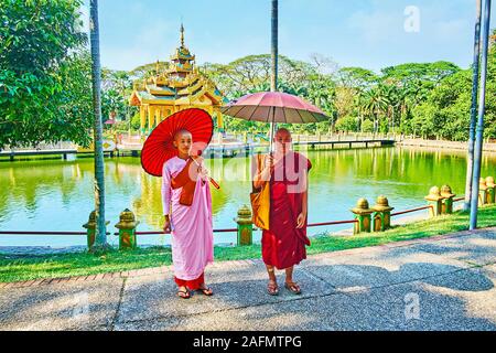 YANGON, MYANMAR - Februar 17, 2018: Der junge bhikkhu Mönch und Bhikkhuni Nonne mit traditionellen Sonnenschirme pose am See des Theingottara Park, am Feb Stockfoto