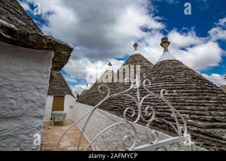 Dächer und Eingang von truli, typisch weiß getünchten zylindrische Häuser in Alberobello, Apulien, Italien mit tollen blauen Himmel mit Wolken, Street View Stockfoto