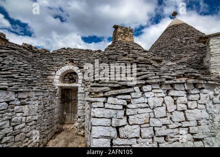 Dächer und Eingang von truli, typisch weiß getünchten zylindrische Häuser in Alberobello, Apulien, Italien mit tollen blauen Himmel mit Wolken, Street View Stockfoto